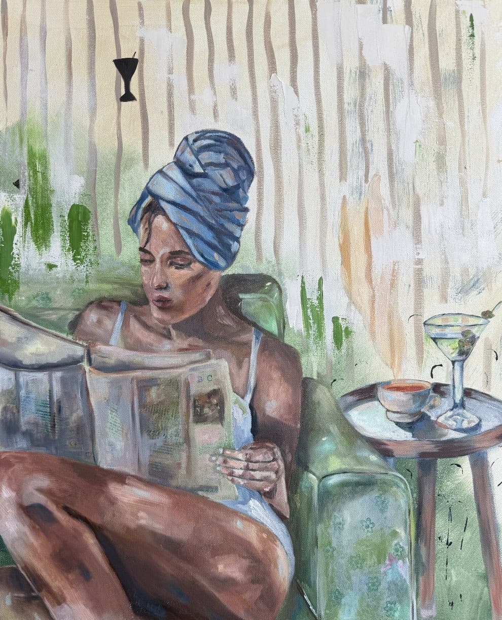 A woman in a blue head towel reads a newspaper in a green chair beside a side table holding tea and a martini.